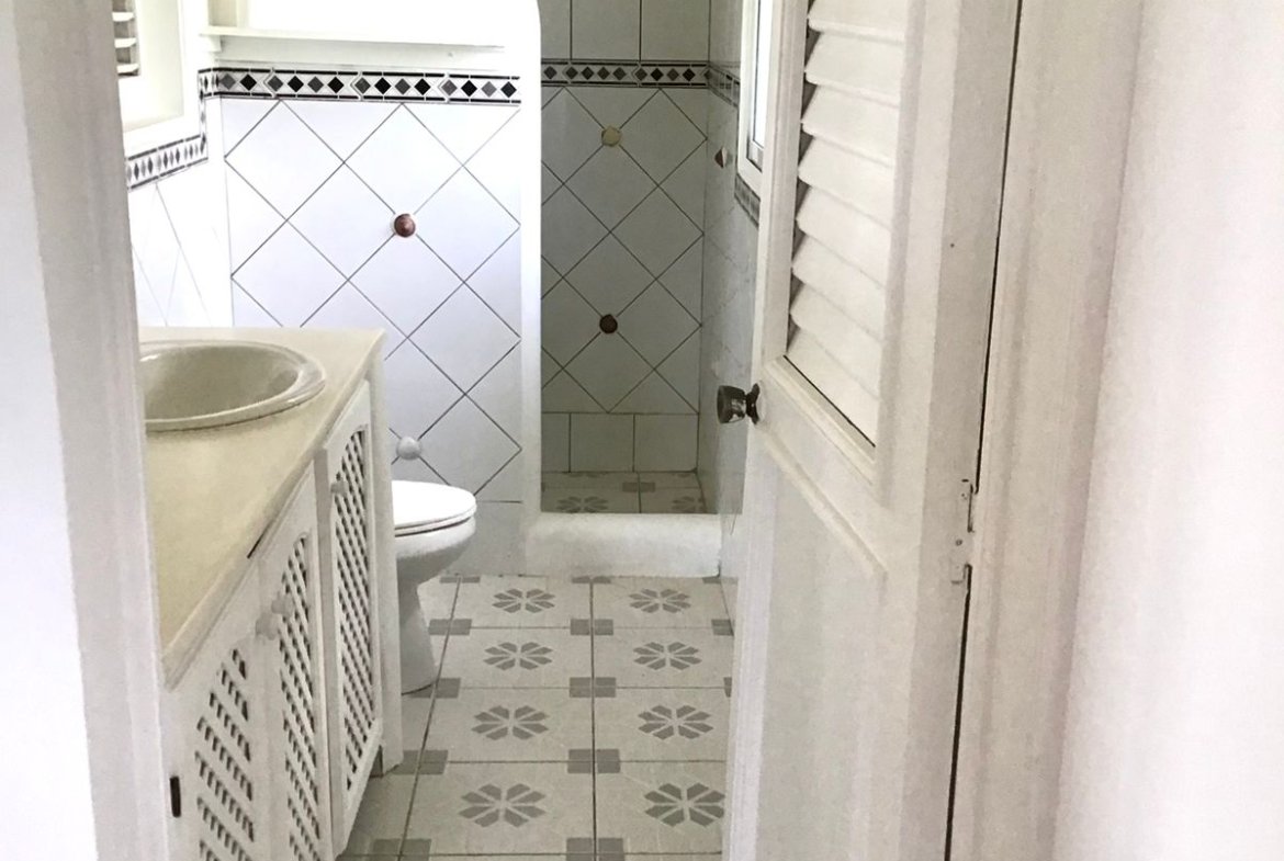 Baño estrecho con ducha y azulejos blancos