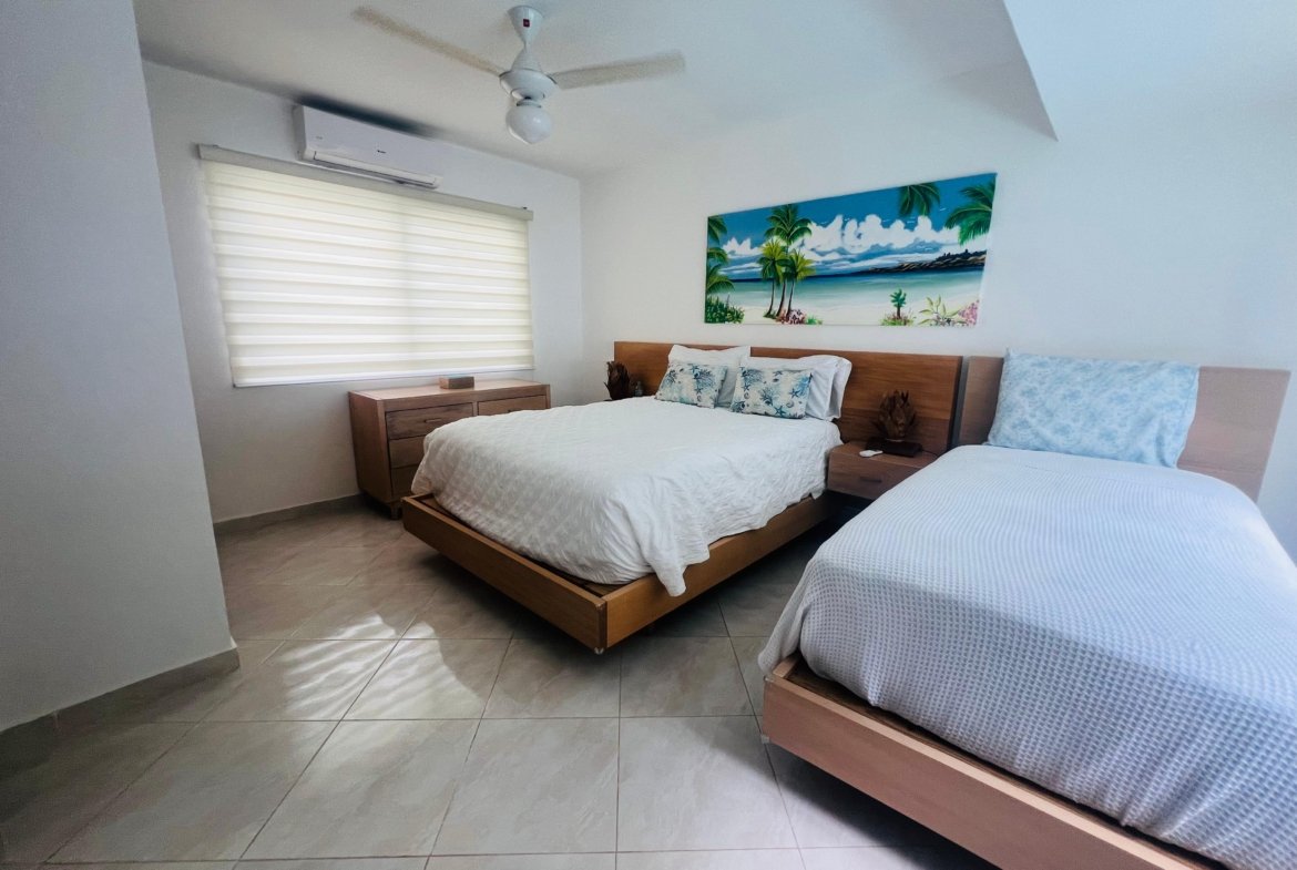 Dormitorio moderno con dos camas y cuadro tropical