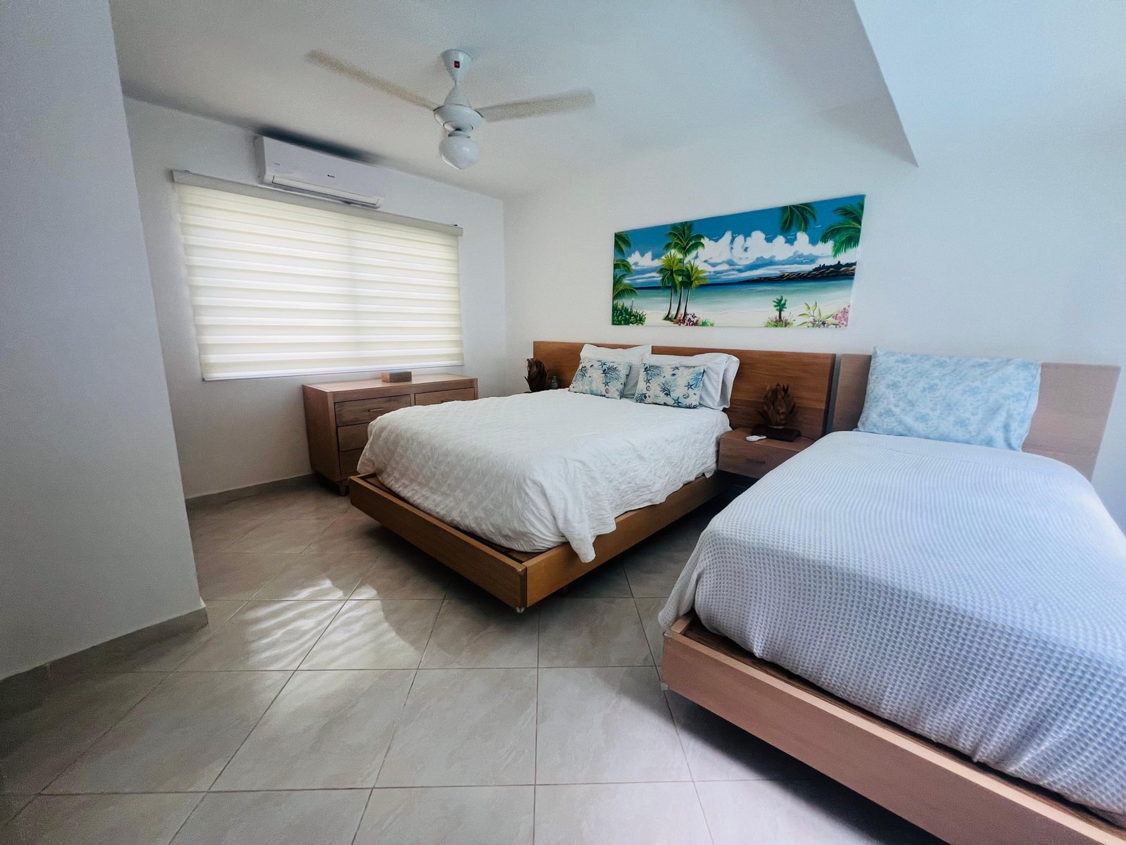 Dormitorio moderno con dos camas y cuadro tropical