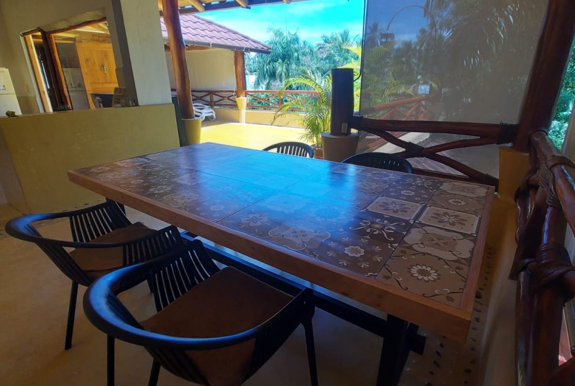 Terraza cubierta con mesa y vistas tropicales