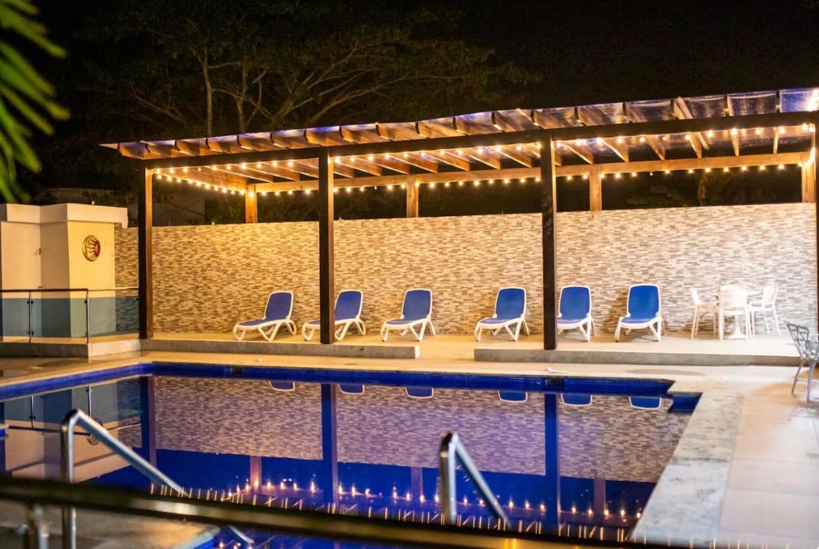 Piscina iluminada de noche con tumbonas azules