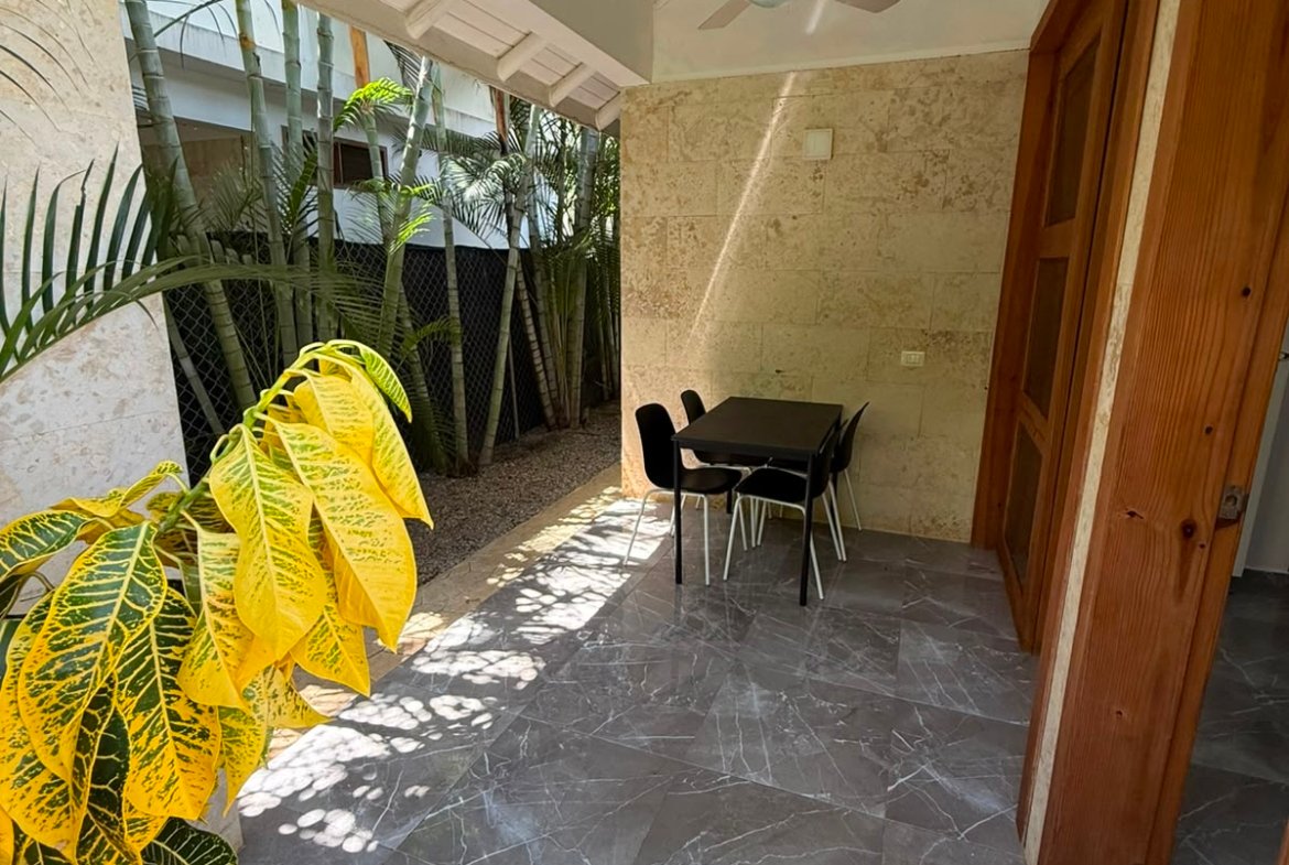 Terraza cubierta con mesa, sillas y plantas tropicales