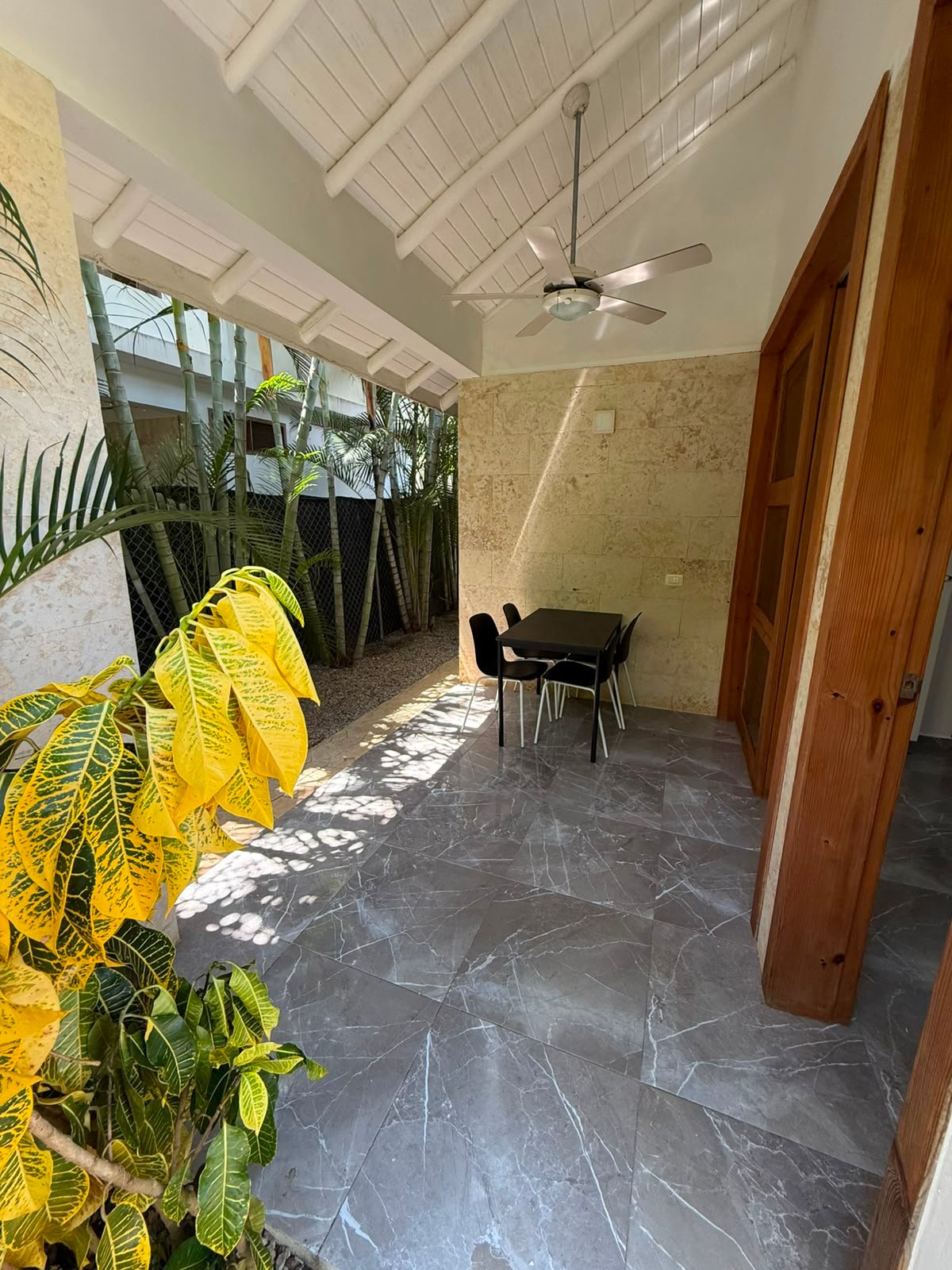 Terraza cubierta con mesa, sillas y plantas tropicales