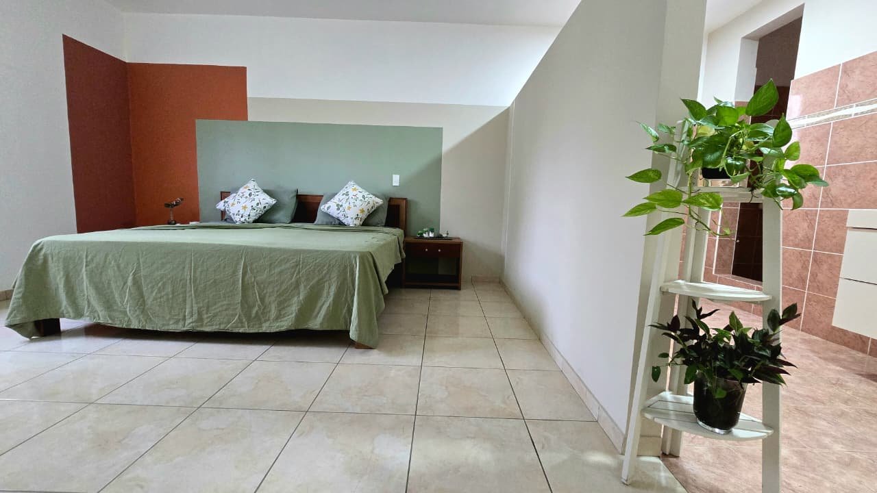 Villa en el limon (9) Dormitorio amplio con cama verde, plantas y baño anexo