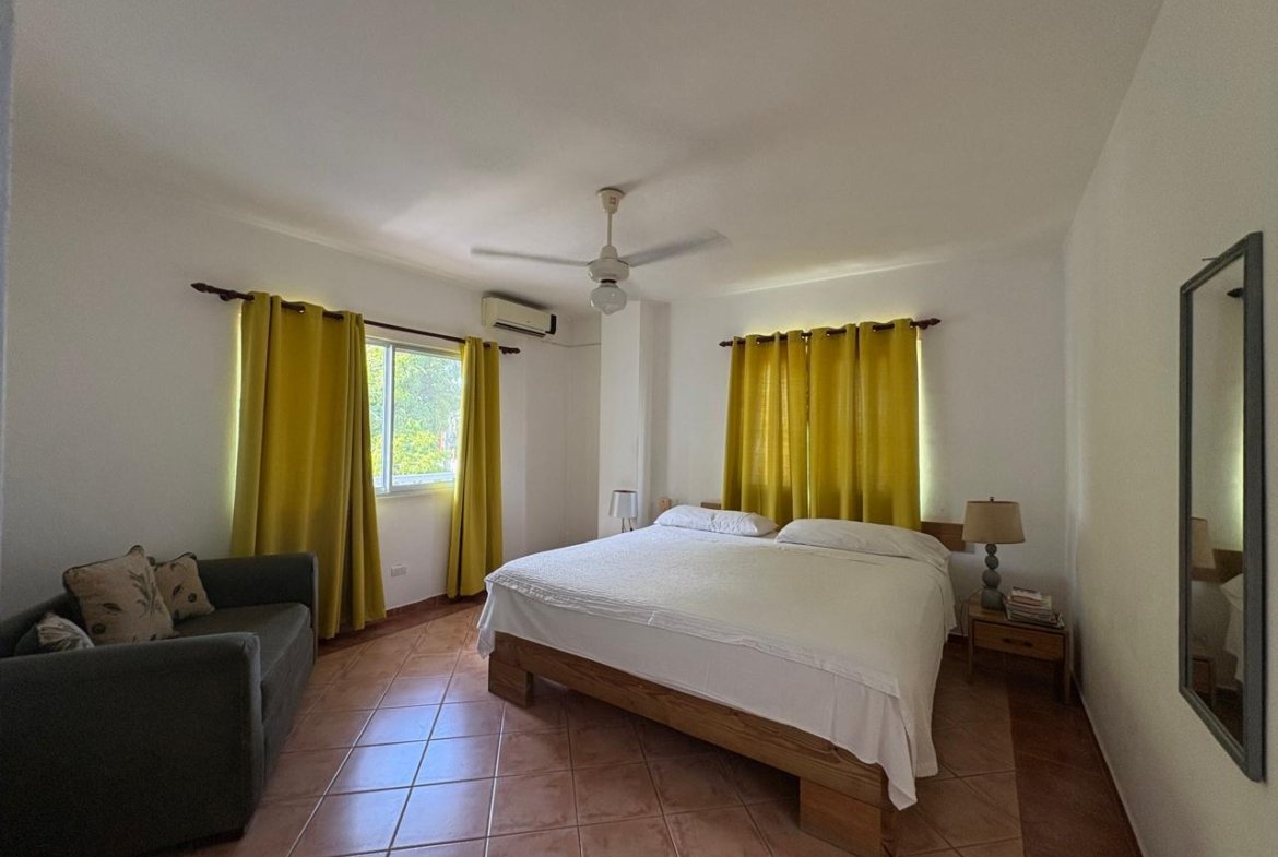 Dormitorio luminoso con cama doble, sofá y cortinas amarillas