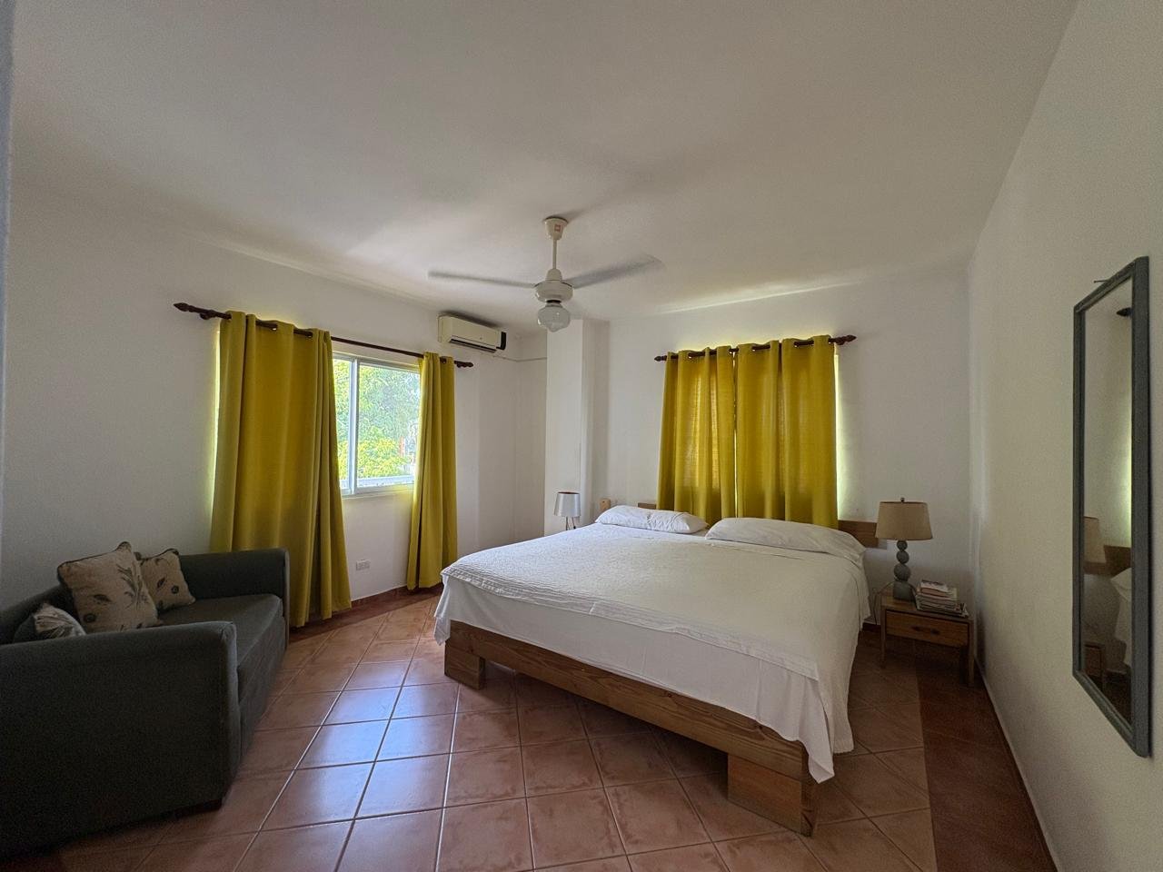 Apartemento Piattini (14) Dormitorio luminoso con cama doble, sofá y cortinas amarillas