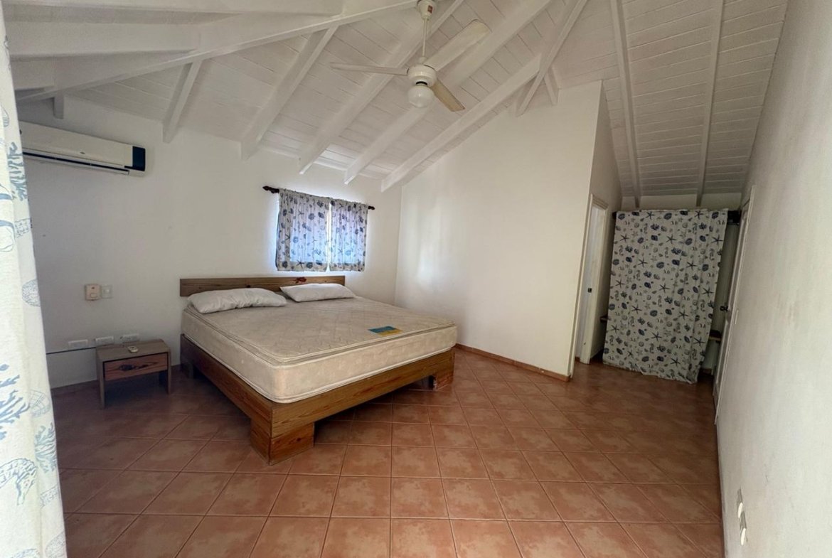 Dormitorio amplio con cama, techo abuhardillado y ventilador