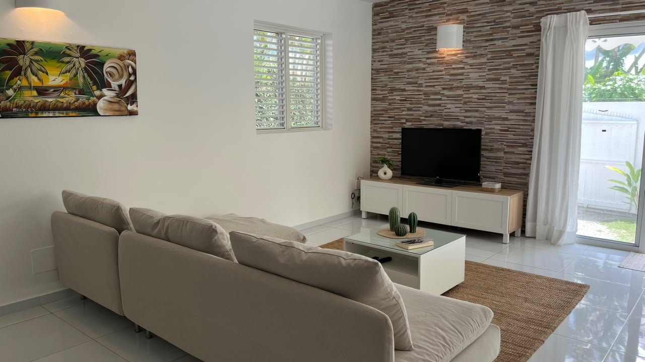 Salón luminoso con sofá, televisión y decoración tropical