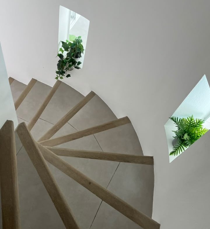 Escalera de caracol con plantas junto a ventanas triangulares