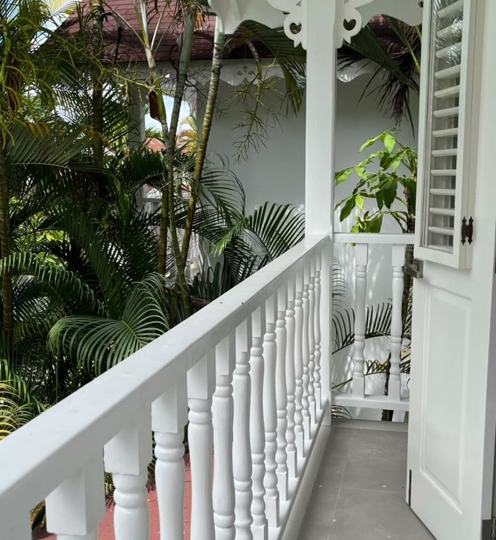 Balcón blanco con persianas junto a palmeras tropicales
