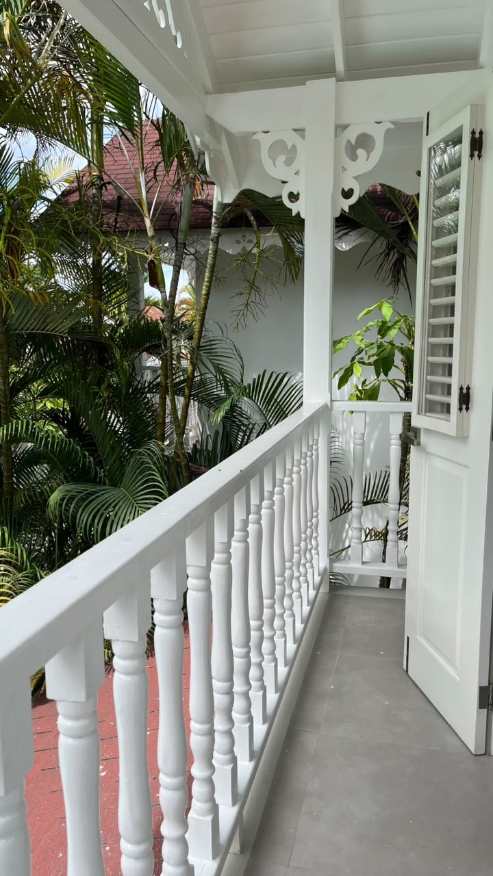 Balcón blanco con persianas junto a palmeras tropicales
