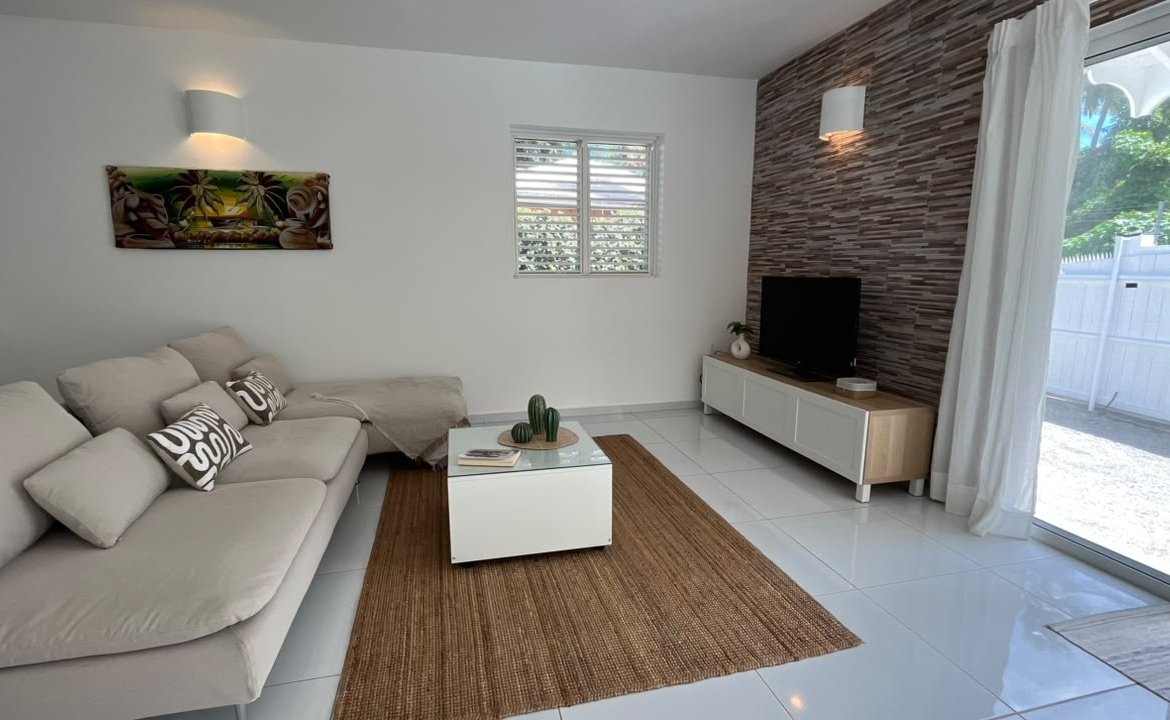 Salón luminoso con sofá beige, televisión y acceso al jardín