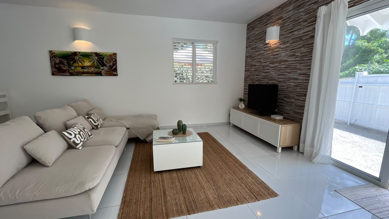 Salón luminoso con sofá beige, televisión y acceso al jardín